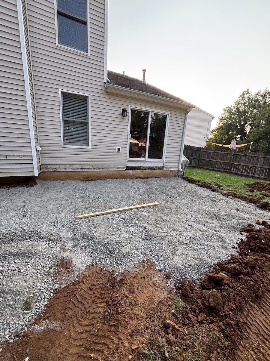 A compacted gravel base laid behind a house with a long leveling board resting across it.